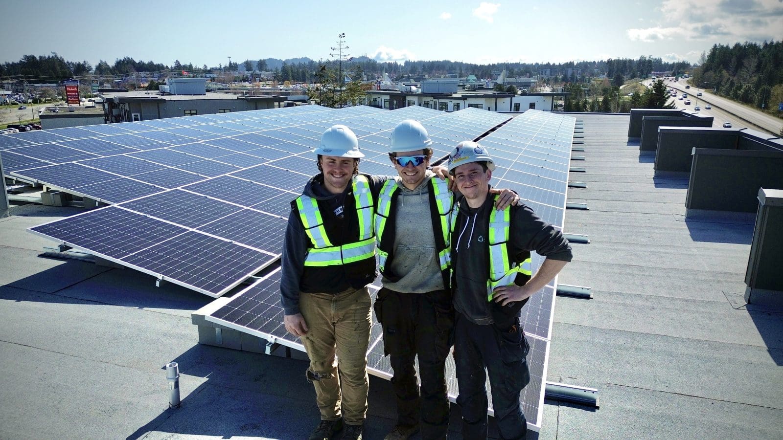 3 shift solar installers standing on the roof of a commercial building, with a solar array in the background