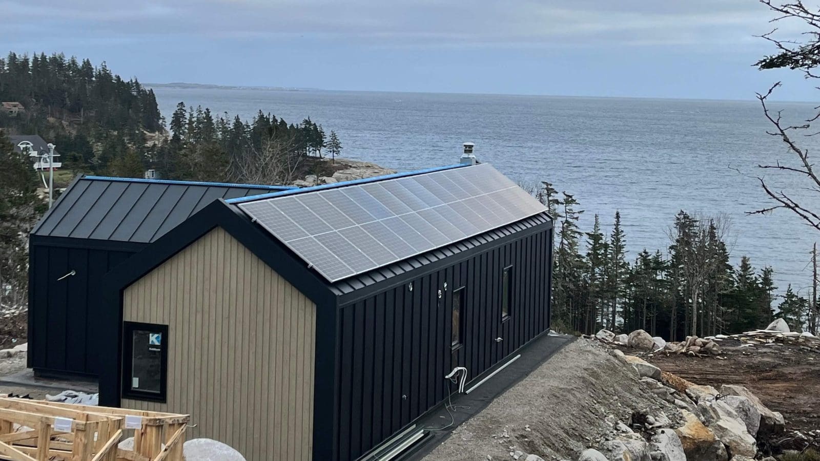 Coastal home with solar panels on the roof. There are trees and the ocean in the background.