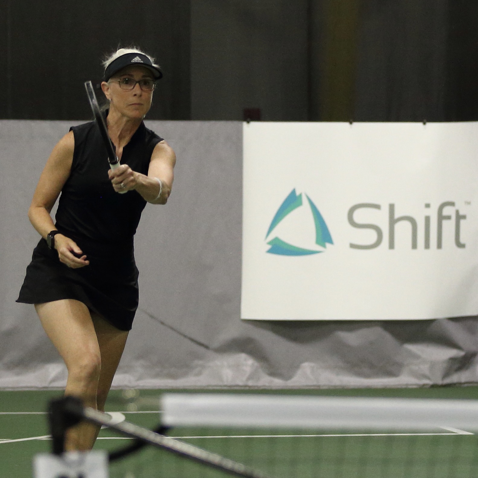 A person playing pickleball in a pickball tournament. The Shift logo is displayed on a sponsorship banner in the background.
